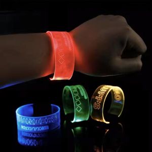 Close up of wrist wearing XL wristband in front of three other LED wristbands that are clasped on a dark table below