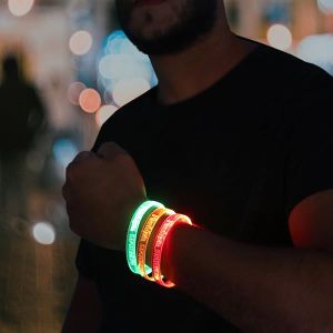 Man in beard wearing black shirt with arm lifted to show three laser engraved LED bracelets glowing green, orange and red