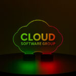 Large acrylic LED table centerpiece with dual bases, featuring a cloud-shaped Cloud Software Group engraved design glowing red and green on a dark tabletop