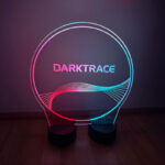 Circular engraved custom branded LED acrylic display sign glowing in pink and teal at a corporate gala