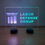 Labor Defense Group LED acrylic table sign glowing teal with dual bases at a corporate networking event